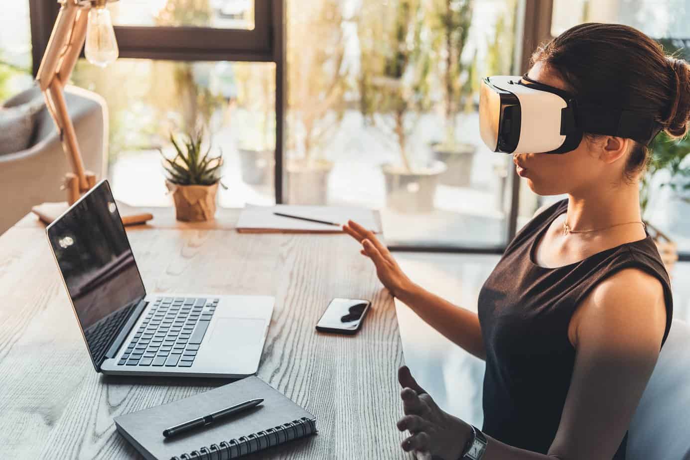 woman wearing virtual reality glasses sitting in front of laptop